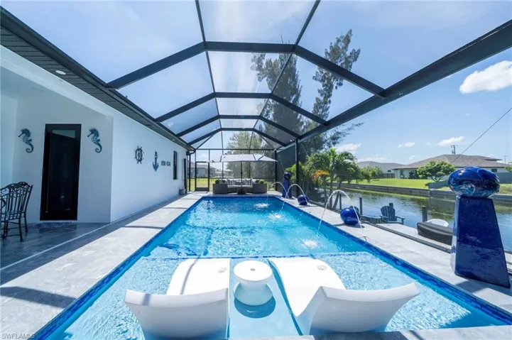 Screened swimming pool with integrated sun shelf, multiple water features, and a view of the adjacent canal