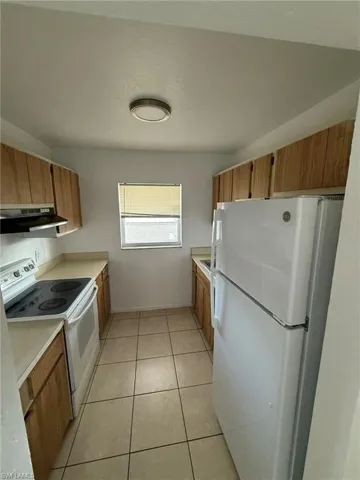Kitchen with white appliances, light countertops, light tile patterned flooring, and brown cabinetry