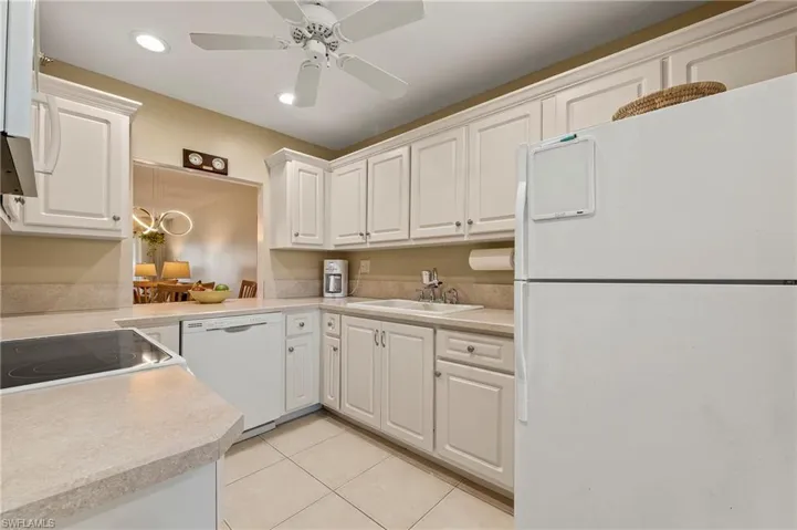 The spacious and modern kitchen features tile floors, white cabinets with crown molding, neutral decor and raised ceiling.