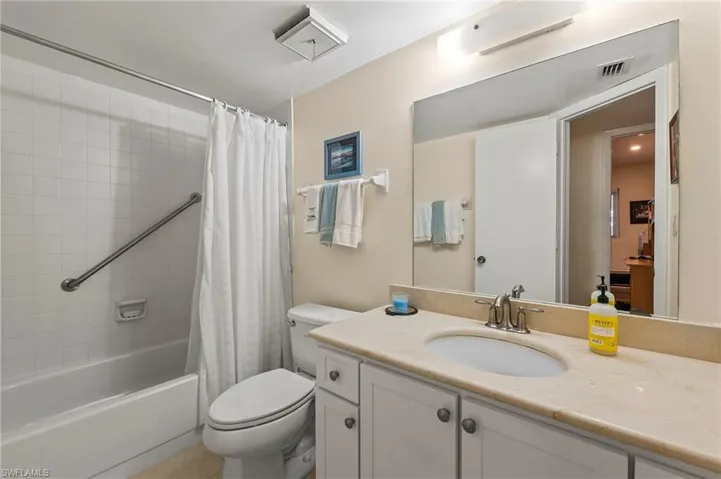 The guest bathroom features Corian counters, white cabinetry, a neutral shower enclosure and large tile floors.