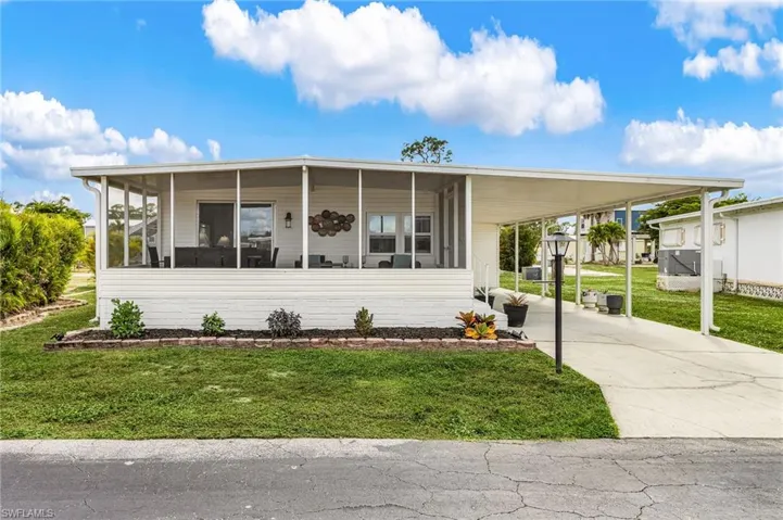 White siding residence featuring a screened-in porch, covered carport, concrete driveway, and a front garden bed with dark mulch
