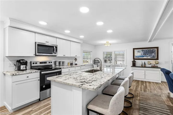 Modern kitchen featuring a large island with seating, stainless steel appliances, granite countertops, recessed lighting, and wood-finish flooring