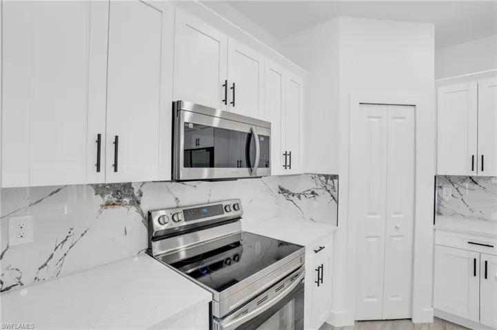 Kitchen featuring tasteful backsplash, light stone counters, white cabinets, and appliances with stainless steel finishes