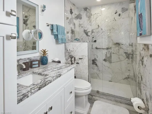 Bathroom with built in linen shelving, seating at vanity, a shower with shower door, and toilet