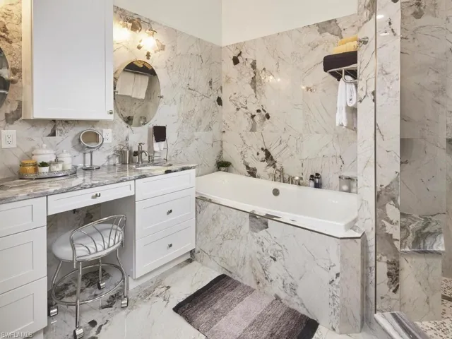 Bathroom featuring a relaxing tiled tub, vanity, and tiled walls