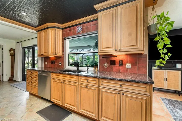 Kitchen with decorative backsplash, dark stone countertops, stainless steel dishwasher, an ornate ceiling, and a sink