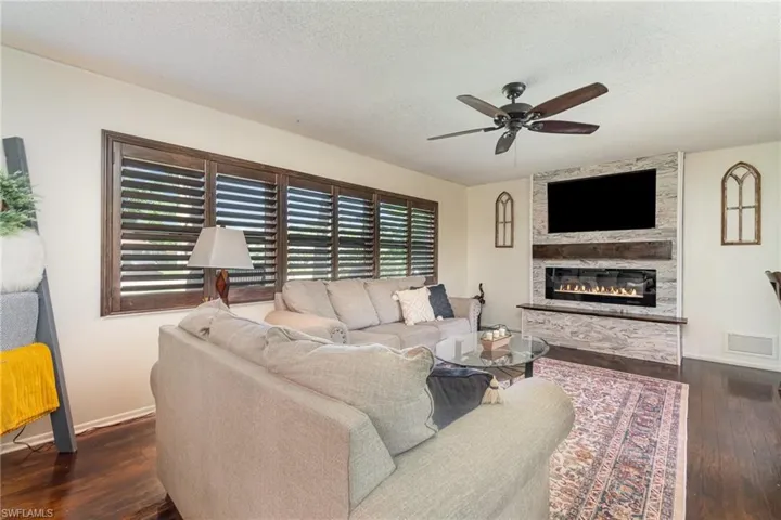 Living room with hardwood / wood-style floors, visible vents, ceiling fan and a stone fireplace,