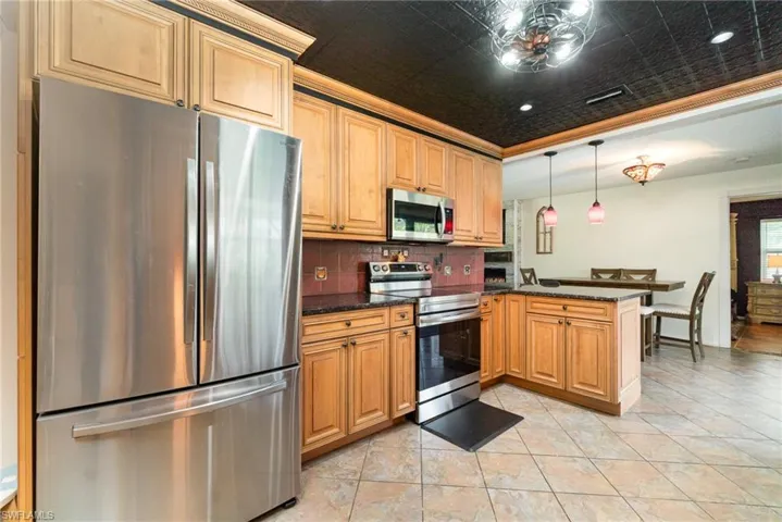 Kitchen with a peninsula, a tray ceiling, stainless steel appliances, decorative backsplash, and decorative light fixtures