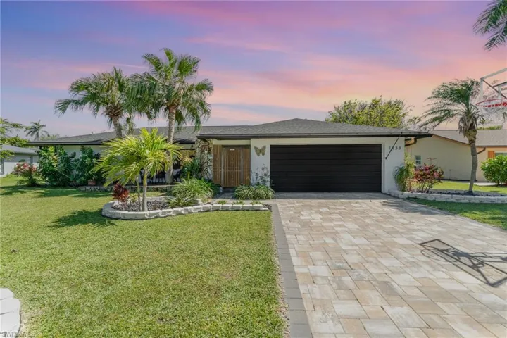 View of front facade with stucco siding, decorative driveway, a front lawn, and an attached garage