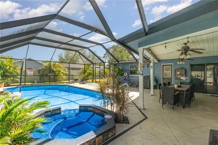 View of pool featuring glass enclosure, a patio, outdoor dining area, and an in ground hot tub
