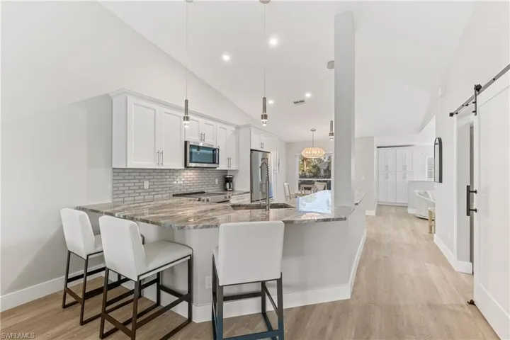 Kitchen featuring a quartz kitchen peninsula, appliances with stainless steel finishes, vaulted ceiling, pendant lighting
