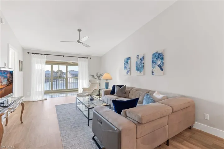 Living room with vaulted ceiling, a water view, light hardwood / wood-style flooring, and ceiling fan