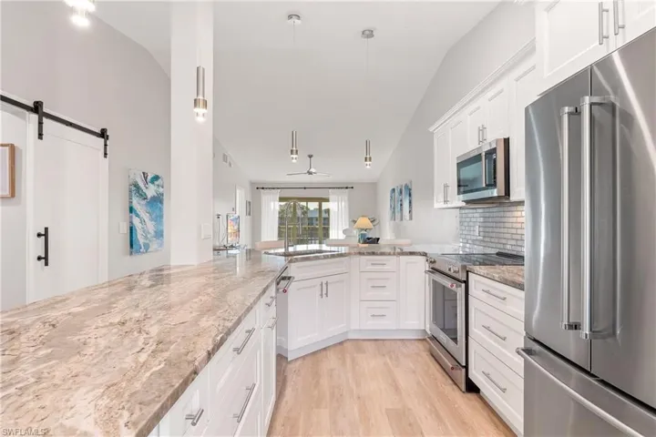 Kitchen featuring decorative light fixtures, modern white cabinets, quartz counters, stainless steel appliances, and vaulted ceiling