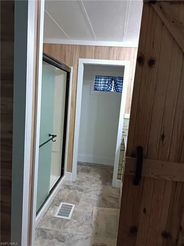 Bathroom with wooden walls, a textured ceiling, and a shower with shower door