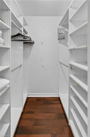 Walk-in closet featuring white shelving units, adjustable shelves, and wood-finish flooring