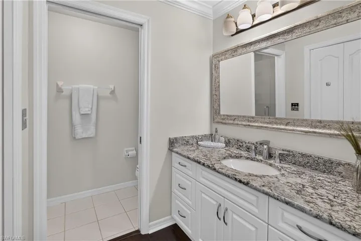 White vanity with shaker-style cabinetry, an integrated sink, and stone countertop