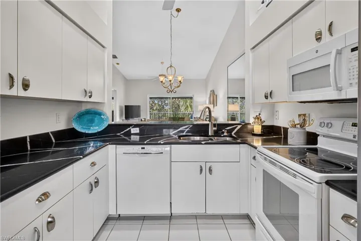 White cabinetry with brushed nickel hardware, black countertops with white veining, white tile flooring, and integrated white appliances