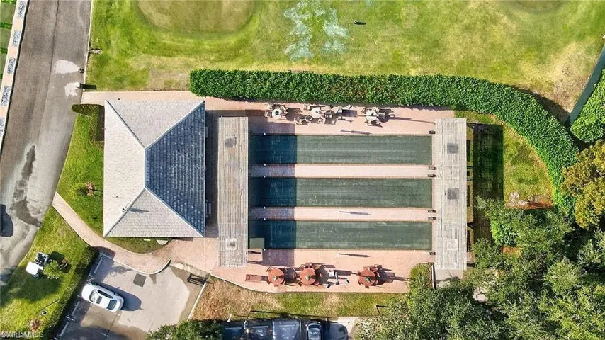 Bocce ball courts with surrounding hardscaping, a partial building with a hip roof, and lush green landscaping
