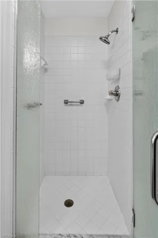 Modern walk-in shower featuring white subway tile walls, a rainfall showerhead with secondary wall-mounted fixture, chrome hardware, a linear drain system integrated into the white tile floor, and a frameless glass enclosure with brushed metal hardware