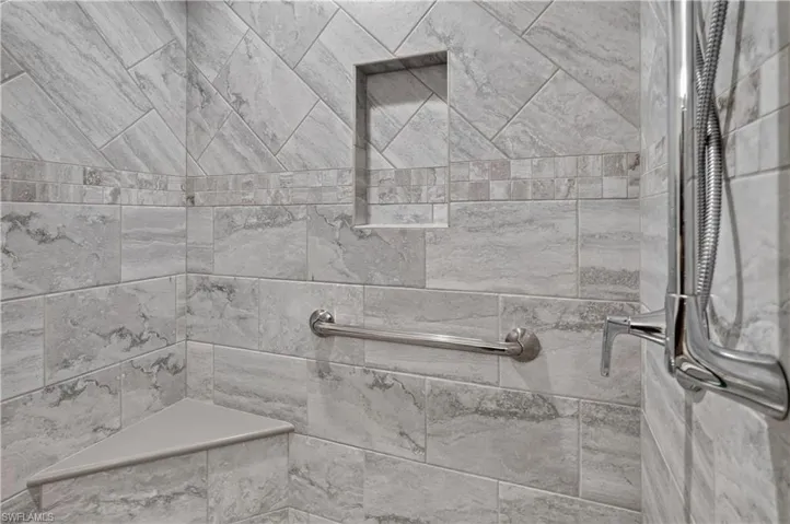 Shower with large format stone-look tile, accent band, built-in niche, and corner bench