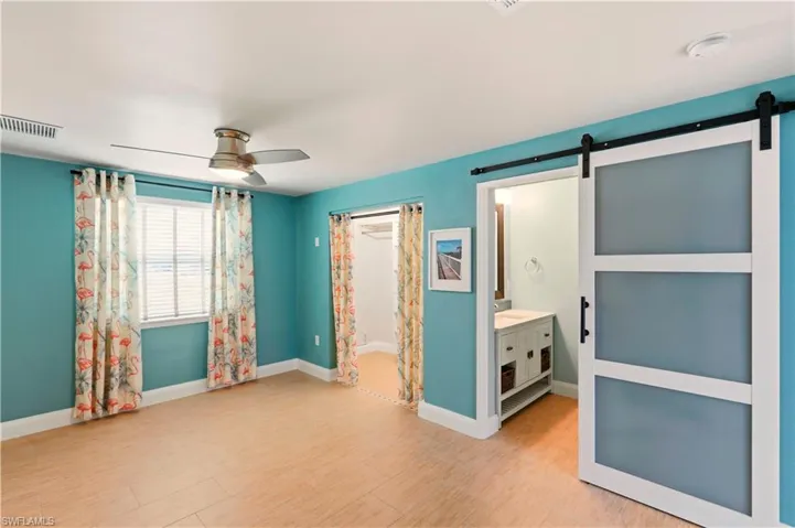 Unfurnished bedroom with a barn door, light wood-style floors, a ceiling fan, and ensuite bath