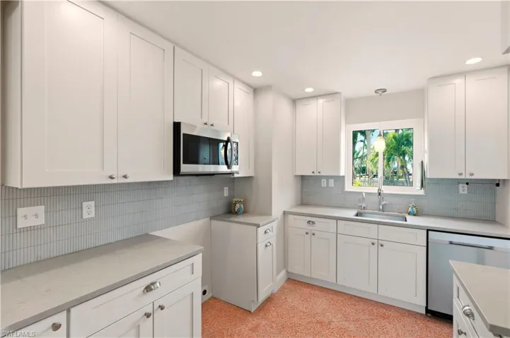 Kitchen featuring white cabinets, stainless steel appliances, decorative light fixtures, light stone countertops, and tasteful backsplash