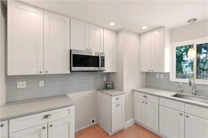 Kitchen featuring white cabinets, stainless steel microwave, backsplash, and light stone countertops