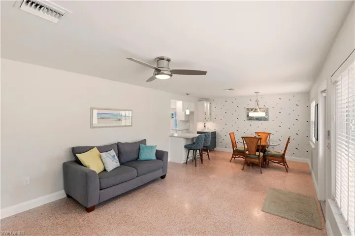 Living room with wallpapered walls, dark aggregate flooring, and a ceiling fan