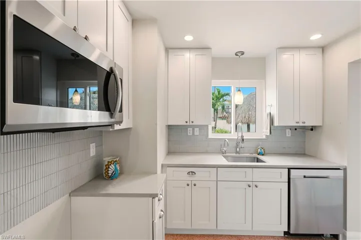 Kitchen featuring stainless steel appliances, white cabinetry, backsplash, light stone countertops, and pendant lighting