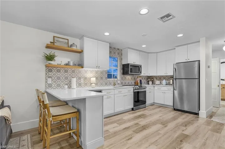 Kitchen with stainless steel appliances, open shelves, white cabinetry, a peninsula, and a breakfast bar area