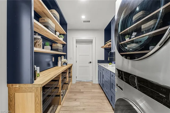 Laundry room featuring light wood-type flooring, stacked washer / dryer, and cabinet space