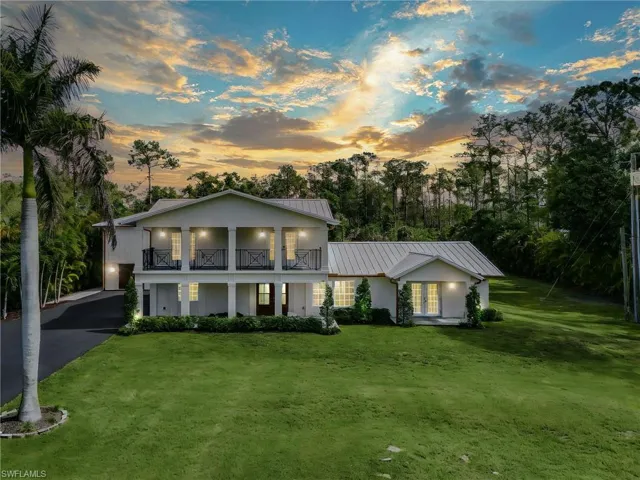 View of front of property featuring a front lawn, driveway, a balcony, and a metal roof