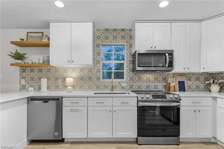 Kitchen featuring appliances with stainless steel finishes, white cabinetry, open shelves, light stone countertops, and tasteful backsplash