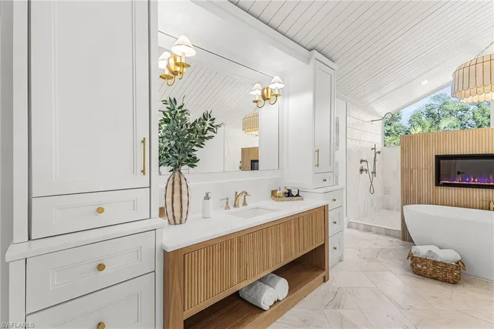Full bathroom featuring lofted ceiling, vanity, a freestanding bath, walk in shower, and light marble finish floors