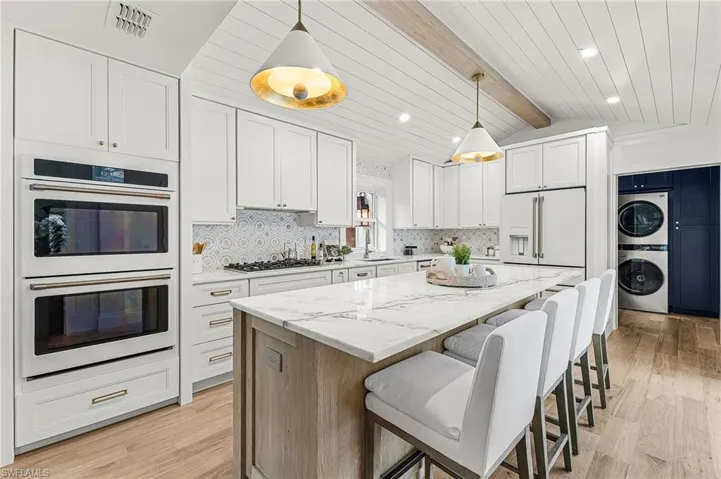 Kitchen with white appliances, white cabinetry, light stone counters, a breakfast bar, and stacked washer / drying machine
