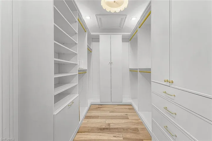 Walk in closet with light wood finished floors and attic access
