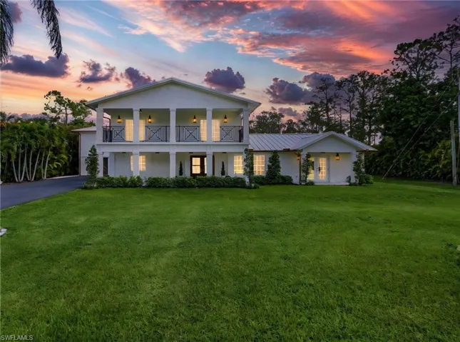 Neoclassical / greek revival house with a front yard, driveway, stucco siding, and covered porch