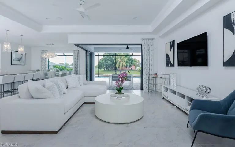 Tiled living room with a tray ceiling, crown molding, and ceiling fan with notable chandelier