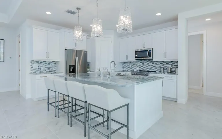 Kitchen with appliances with stainless steel finishes, decorative backsplash, an island with sink, and white cabinets