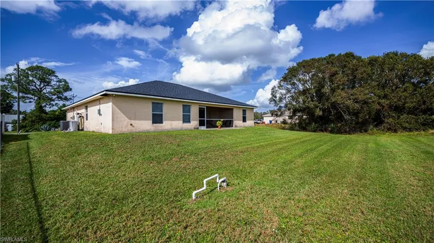 Back of property with central air condition unit and a lawn