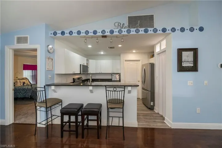 Kitchen with white cabinetry, appliances with stainless steel finishes, kitchen peninsula, lofted ceiling, and dark wood-type flooring