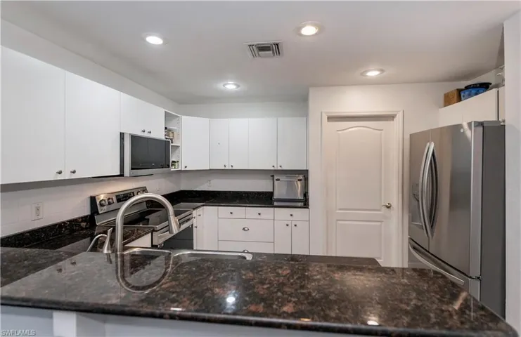 Kitchen with white cabinetry, kitchen peninsula, appliances with stainless steel finishes, and dark stone countertops