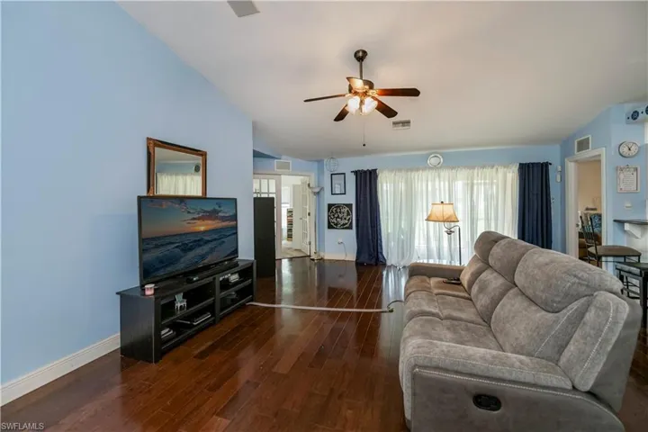 Living room with dark wood-type flooring, ceiling fan, and lofted ceiling