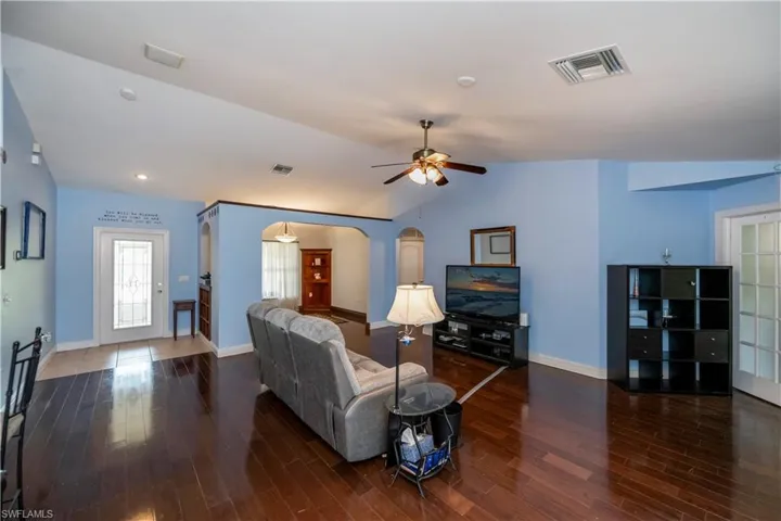Living room with dark hardwood / wood-style flooring, lofted ceiling, and ceiling fan