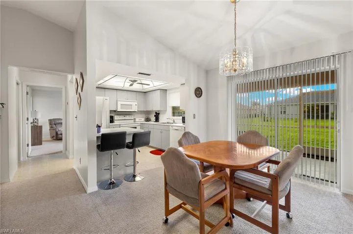 Dining space featuring high vaulted ceiling, sink, light carpet, and a notable chandelier