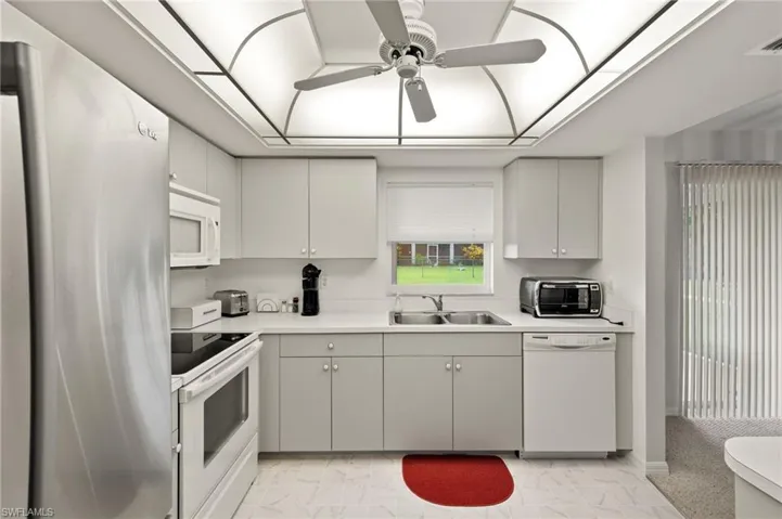 Kitchen with sink, light tile patterned flooring, ceiling fan, and white appliances