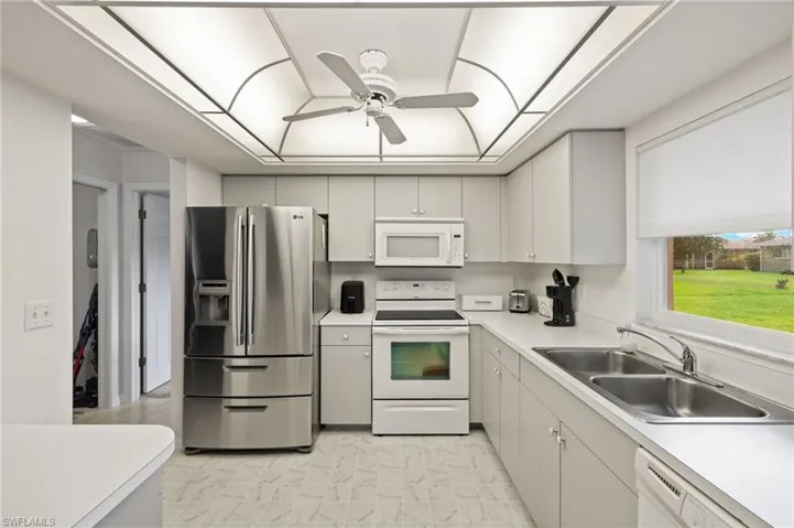 Kitchen featuring white cabinetry, white appliances, light tile patterned floors, ceiling fan, and sink