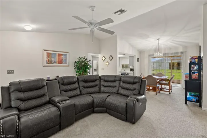 Carpeted living room featuring lofted ceiling and ceiling fan with notable chandelier