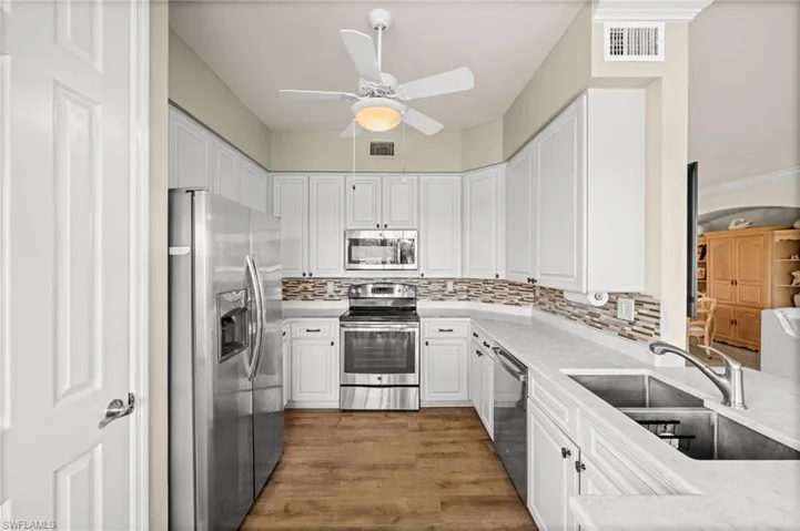 Kitchen featuring appliances with stainless steel finishes, tasteful backsplash, white cabinetry, dark wood-style flooring, and light stone countertops