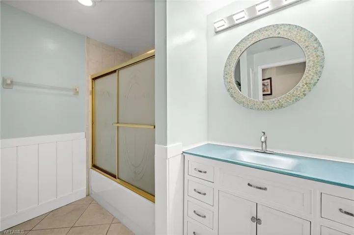 Full bathroom with bath / shower combo with glass door, light tile patterned floors, vanity, and a wainscoted wall
